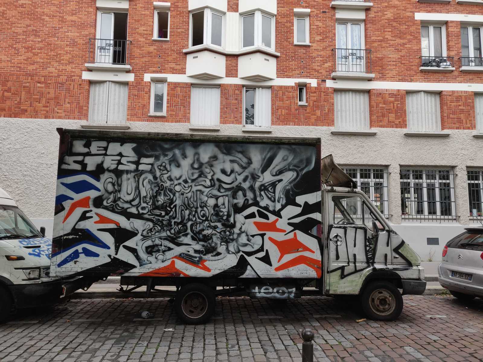 Graffiti STESI und LEK75019 Graffiti STESI und LEK75019 auf einem Lastwagen, abstrakter Schirftzug trifft auf eckig, Graffiti-Legenden von Paris, Backstein-Architektur im Hintergrund