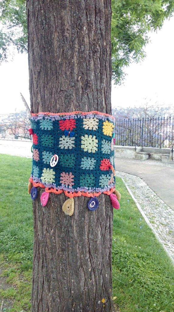 Urban Knitting Köln Subkultur feminines Streetart urbane Kunst Raumaneignung Kunst öffentlicher Raum Strick-Graffiti um einen Baum mit Peace-Anhänger